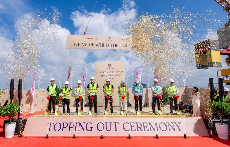The Eaton Park topping-out ceremony on the roof of the final two towers: nine people in hard hats and high-visibility vests hold gold spades behind a stand reading Topping Out Ceremony.