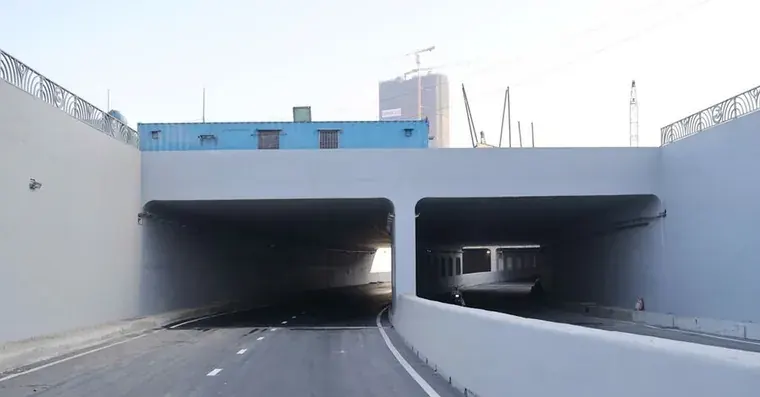 The twin portals of the newly opened HC1-02 underpass at the An Phu Interchange, with fresh road markings and a tower crane on the skyline behind.