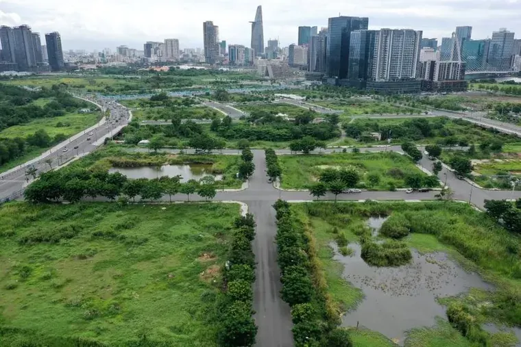 Aerial photograph of vacant, road-gridded land in the Thu Thiem new urban area, with the Ho Chi Minh City skyline and the Saigon River behind.