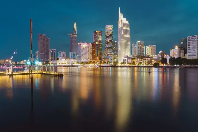 The District 1 skyline at night seen across the Saigon River from the Thu Thiem bank, the towers reflected in the water.