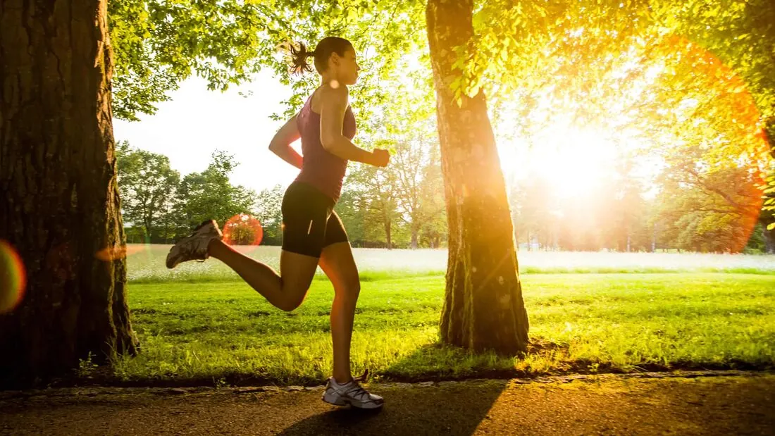 A woman running along a tree-lined path at sunrise